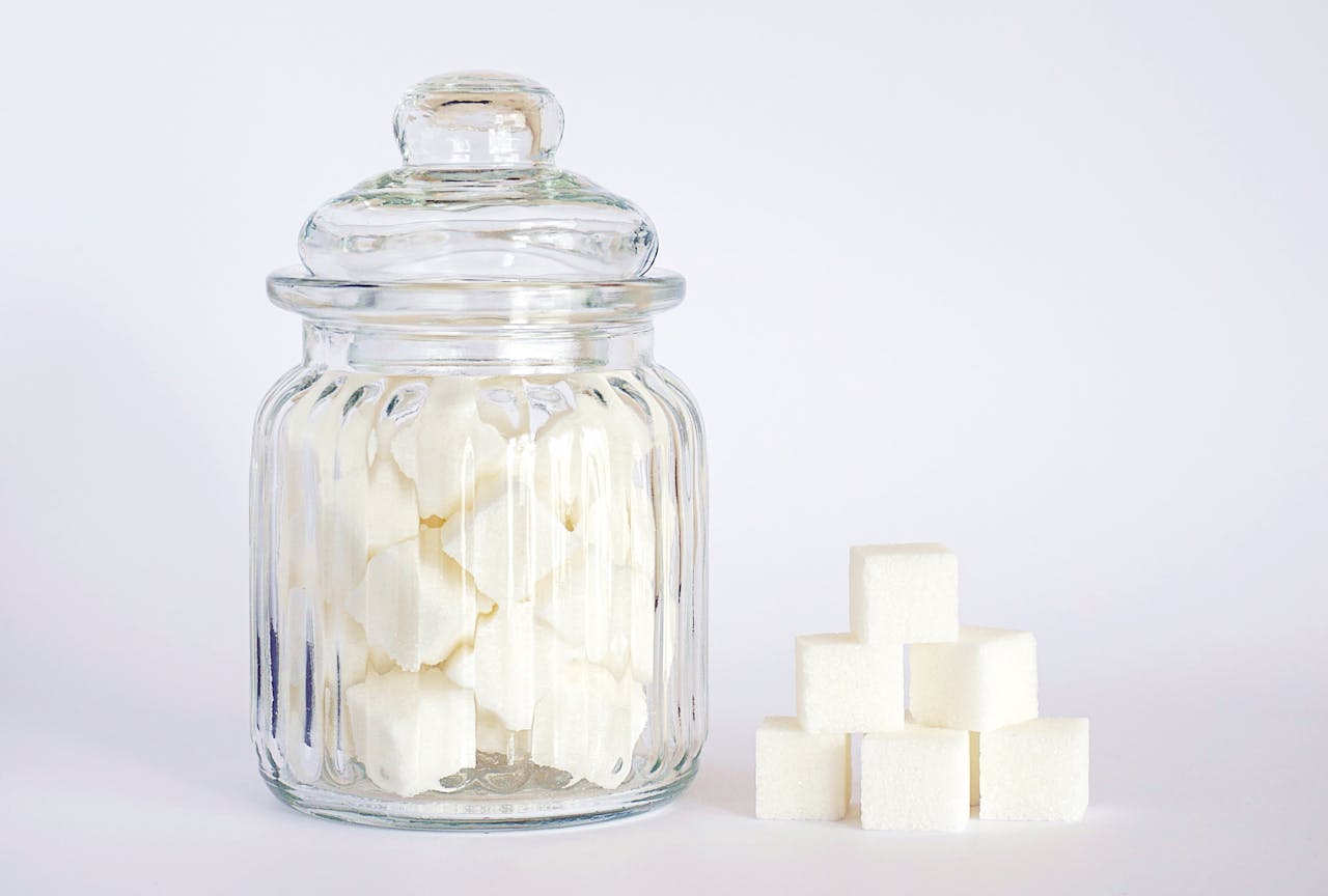 about-us A clear glass jar filled with sugar cubes next to stacked cubes on a white background.